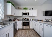 Thumbnail 2 of 15 - A kitchen with white cabinets and a wooden floor.