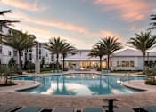 Thumbnail 22 of 51 - A large swimming pool surrounded by palm trees and a building in the background at Enclave at 3230 Apartments, South Daytona, FL, 32119