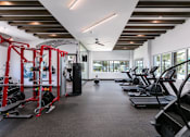 Thumbnail 42 of 51 - A gym with a variety of equipment including treadmills, weights, and a ceiling fan at Enclave at 3230 Apartments, South Daytona, FL