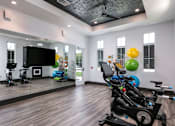 Thumbnail 44 of 51 - A room with a wooden floor and a ceiling fan, equipped with exercise bikes and a television at Enclave at 3230 Apartments, South Daytona, FL