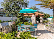 Thumbnail 21 of 51 - a patio with tables and chairs and a blue umbrella at Enclave at 3230 Apartments, South Daytona, 32119