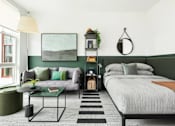 Thumbnail 6 of 19 - A bedroom with a bed, a couch, a table, and a plant.
