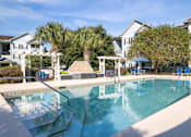 Thumbnail 18 of 26 - a swimming pool with blue chaise lounge chairs and palm trees in the background at Magnolia Village Apartments, Jacksonville, FL