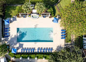 Thumbnail 19 of 26 - arial view of a swimming pool with chaise lounge chairs and trees in the background at Magnolia Village Apartments, Jacksonville, Florida