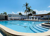 Thumbnail 7 of 12 - A large outdoor swimming pool with a sun lounger area and palm trees in the background.