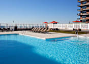 Thumbnail 31 of 43 - a swimming pool with chairs and umbrellas next to a hotel at 10 West Apartments, Long Beach, NY