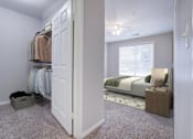 Thumbnail 17 of 21 - A bedroom with a bed, nightstand, and a closet with clothes.