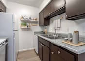 Thumbnail 23 of 26 - A small kitchen with a white refrigerator and brown cabinets.