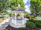 Thumbnail 17 of 40 - A gazebo with a white railing and a black roof is surrounded by green bushes and trees.