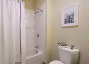 Thumbnail 16 of 35 - A white toilet sits next to a white bathtub in a bathroom at Axis at Lakeshore Apartments, Bridgewater, MA