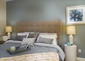 Thumbnail 19 of 35 - A bed with a grey headboard and a grey blanket with a gold pattern on it at Axis at Lakeshore Apartments, Bridgewater