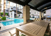 Thumbnail 36 of 72 - A wooden table is in the foreground of a patio with a pool.