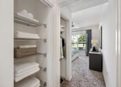 Thumbnail 35 of 38 - A white closet with towels on shelves and a bedroom with a bed and a dresser in the background.