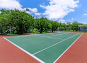 Thumbnail 5 of 42 - a tennis court with trees and a blue sky with clouds
