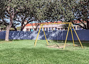 Thumbnail 8 of 42 - a yellow swing set in a playground with trees