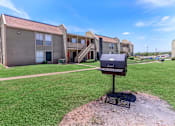 Thumbnail 5 of 37 - A barbecue grill is in the foreground of a grassy area in front of apartment buildings.