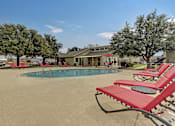 Thumbnail 12 of 43 - a pool with red chairs and a building in the background