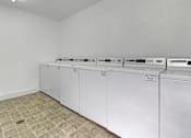 Thumbnail 15 of 43 - a row of washes and dryers in an empty laundry room