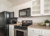 Thumbnail 24 of 34 - A black refrigerator sits next to a black microwave in a kitchen with white cabinets.
