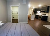 Thumbnail 37 of 39 - A bedroom with a bed in the foreground and a kitchen in the background.