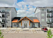 Thumbnail 28 of 37 - A modern apartment complex with a central building and parking lot.