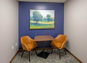 Thumbnail 27 of 37 - A painting of a tree in a field hangs on a blue wall above a table with two chairs.