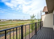 Thumbnail 23 of 36 - A balcony with a black railing overlooks a field with power lines in the distance.
