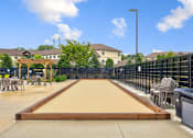 Thumbnail 33 of 36 - A shuffleboard court is located in a courtyard surrounded by chairs and a fence.