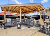 Thumbnail 32 of 36 - A patio with a grill and chairs under a wooden roof.