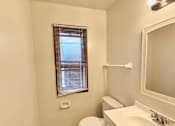 Thumbnail 6 of 11 - A white bathroom with a toilet, sink, and window at Root River Apartments, Wisconsin