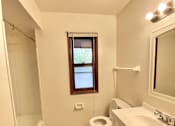 Thumbnail 3 of 11 - A bathroom with a toilet, sink, and a window at Root River Apartments, Greendale, 53129