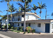 Thumbnail 6 of 16 - A white two-story house with a blue door and windows surrounded by palm trees.