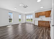 Thumbnail 12 of 24 - A spacious room with wooden flooring and a kitchen area with wooden cabinets.