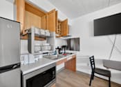 Thumbnail 20 of 23 - A kitchen with a refrigerator, microwave, oven, sink, and a chair.