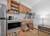 Thumbnail 18 of 23 - A kitchen with a refrigerator, microwave, oven, sink, and a table with a lamp.