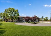 Thumbnail 31 of 32 - A large grassy area in front of a building with a tree on the left.