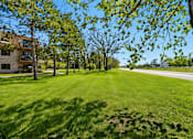 Thumbnail 26 of 32 - A grassy field with trees and a building in the background.