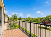 Thumbnail 11 of 32 - A balcony with a black railing overlooks a green lawn and trees.