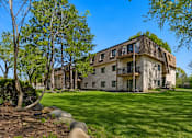 Thumbnail 23 of 32 - A large, two-story house with a balcony on the second floor is surrounded by a grassy lawn and trees.