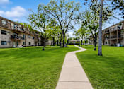 Thumbnail 25 of 32 - A walkway leads through a grassy area between apartment buildings.