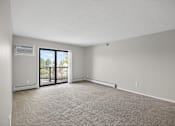 Thumbnail 6 of 32 - A room with a carpeted floor and a sliding glass door leading to a balcony.