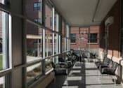 Thumbnail 8 of 23 - A long hallway with black chairs and windows on the side.