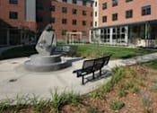 Thumbnail 2 of 23 - A statue is in the middle of a courtyard with a bench to the right.