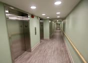 Thumbnail 21 of 28 - A long hallway with elevators on the left and a yellow line on the right.