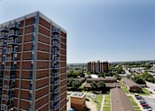 Thumbnail 9 of 28 - A tall brick building with many windows is in the foreground of a cityscape.