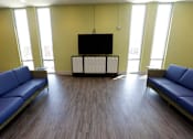 Thumbnail 27 of 28 - A room with a television and two blue couches.