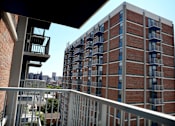 Thumbnail 6 of 28 - A tall red brick building with balconies and a view of the city in the distance.