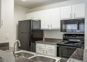 Thumbnail 16 of 23 - A black refrigerator is in a kitchen with granite countertops and stainless steel appliances.