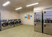 Thumbnail 16 of 23 - Laundry room with a row of washing machines and refrigerators at 500 Fifth Apartments, Tennessee, 37219