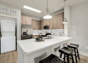 Thumbnail 13 of 37 - A modern kitchen with a white countertop and black bar stools at The Ashton at East Park Apartments, Georgia